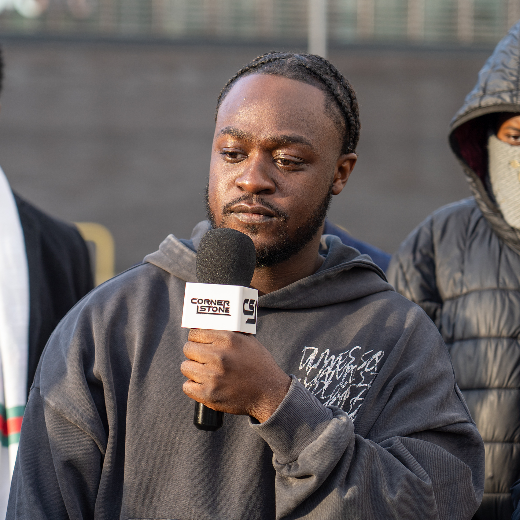 Artist in a grey hoodie holding a Cornerstone microphone outdoors