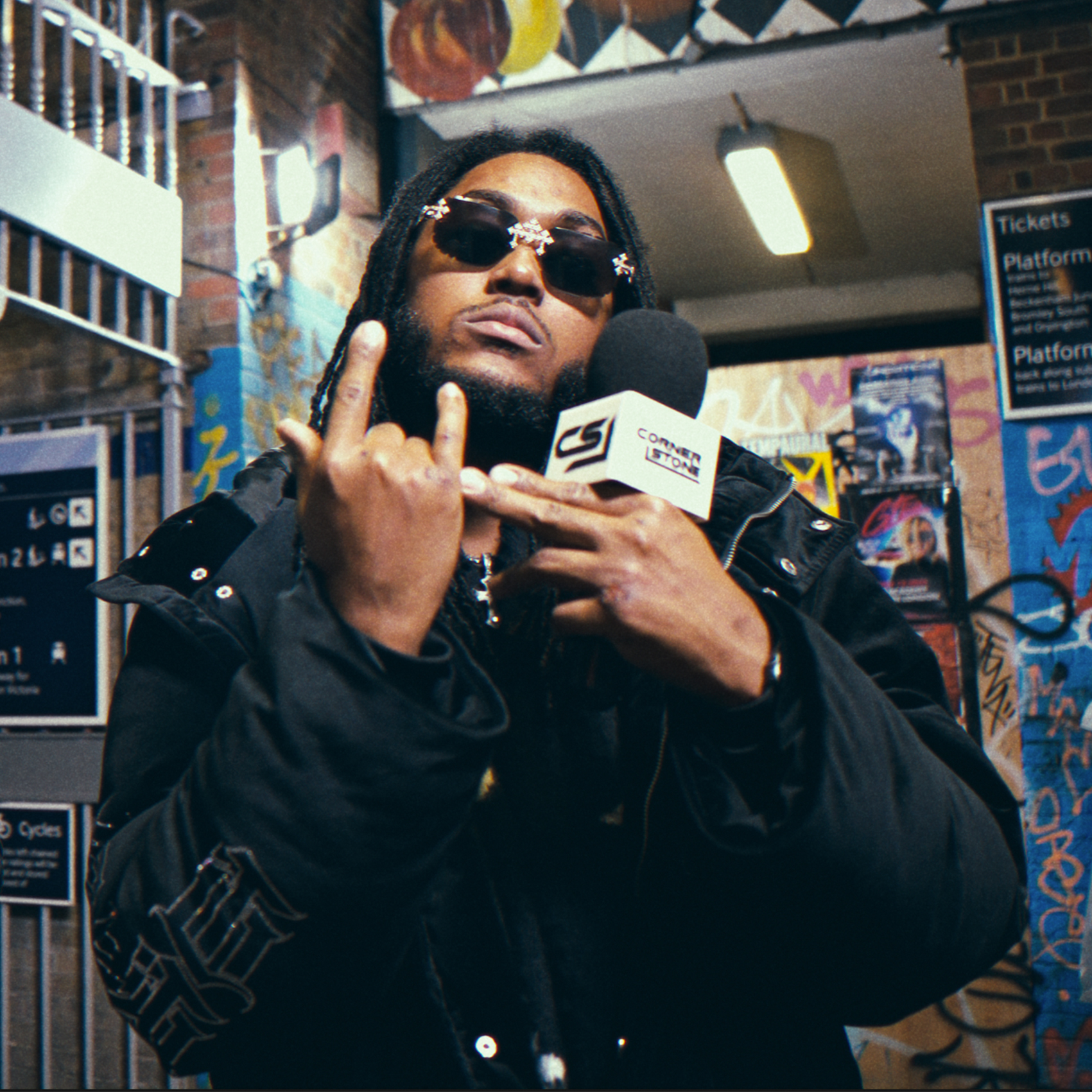 Artist in sunglasses holding a Cornerstone microphone at a railway station