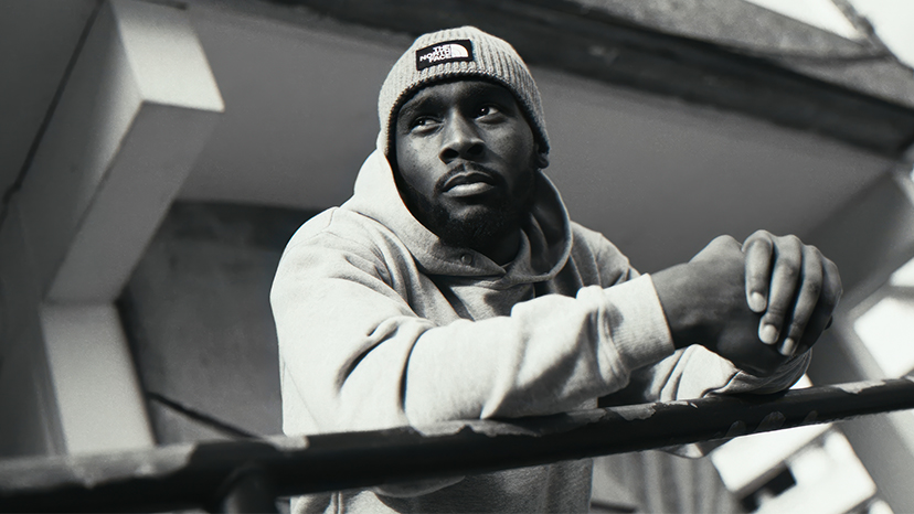Black and white portrait of a man in a beanie leaning on a railing
