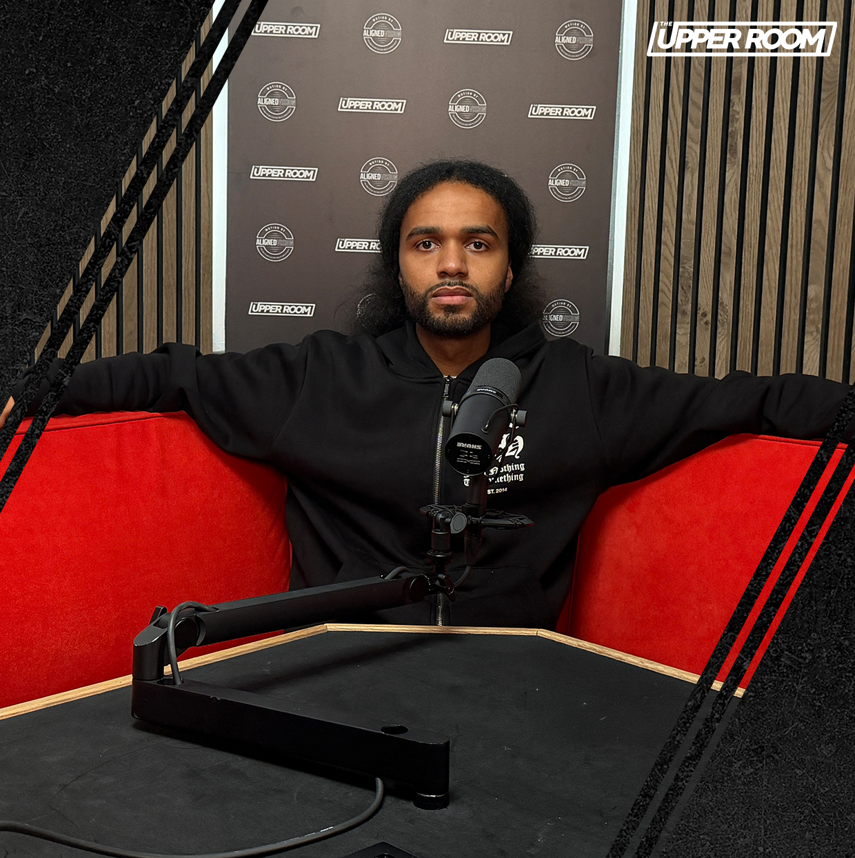 Guest seated on a red sofa at a podcast microphone in The Upper Room studio