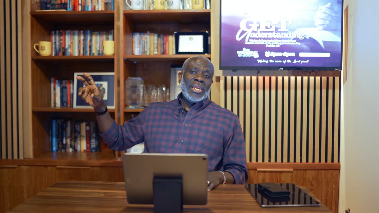 A man in a checked shirt speaking to camera from a desk, with a church event graphic on the TV screen behind him
